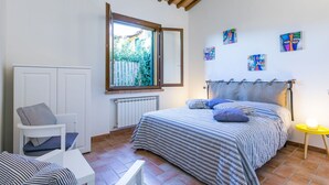 Ein Schlafzimmer mit einem Bett, einem Sessel, einem kleinen Tisch, einem Fenster und Bildern an der Wand.