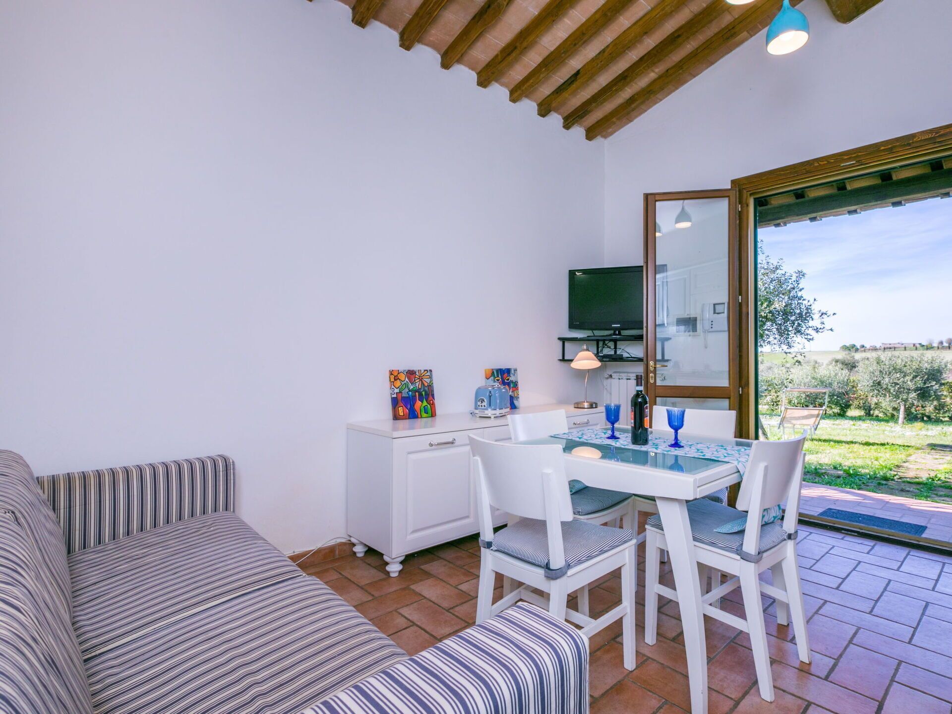 A cozy room with a sofa, a dining table with chairs, a TV, and a view of the outdoors.