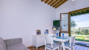 Ein gemütliches Zimmer mit einer Couch, einem Esstisch mit Stühlen, einem Fernseher und Blick ins Freie.