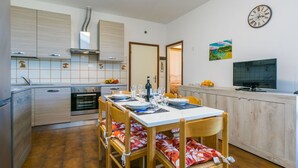 A compact kitchen with modern appliances, a dining table set for four, and a TV on the wall. - Beautiful apartment for 5 guests with WIFI, TV and balcony (Cecina)