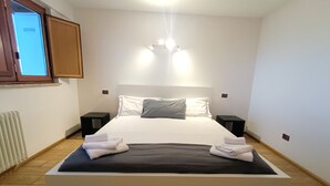 A neatly made bed with white linens and two pillows, a bedside table with a lamp, and a window with a view of the outside. - [10 minutes from city center] Luxury Penthouse with Terrace and Panoramic View (Roma)