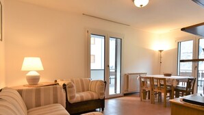 Ein Wohnzimmer mit einer Couch, einem Tisch und Stühlen. Auf der Couch steht eine Stehlampe und auf dem Tisch eine Tischlampe.