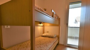 Ein kleiner, kompakter Raum mit Etagenbett und Einzelbett, ausgestattet mit einem schlichten Holzboden und einem kleinen Fenster.