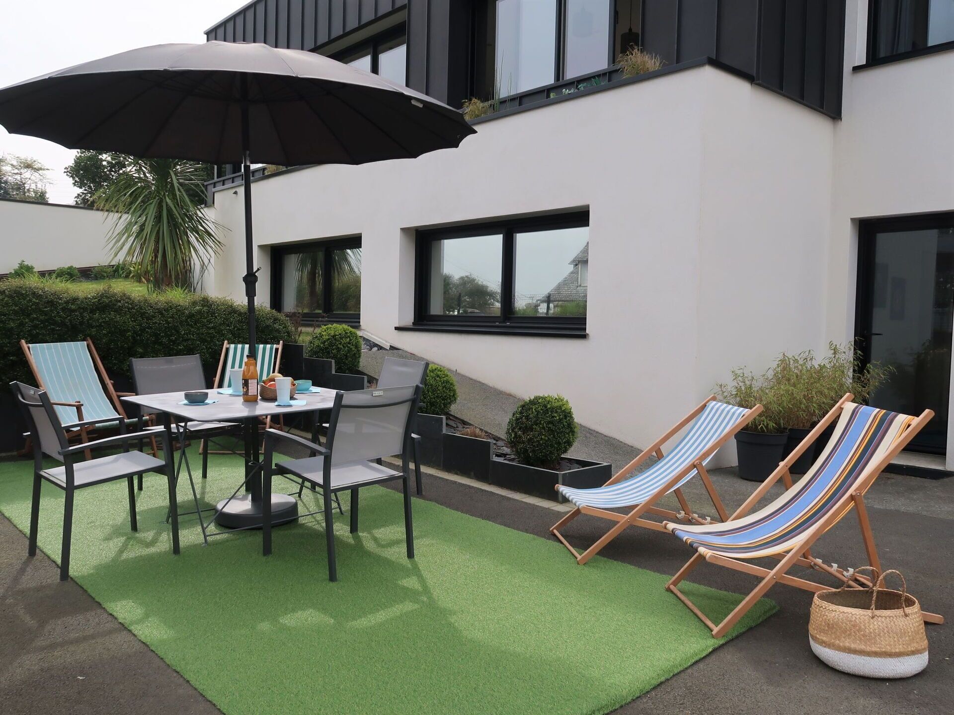 Une terrasse avec une table et des chaises, un fauteuil de jardin à rayures et un grand parasol.