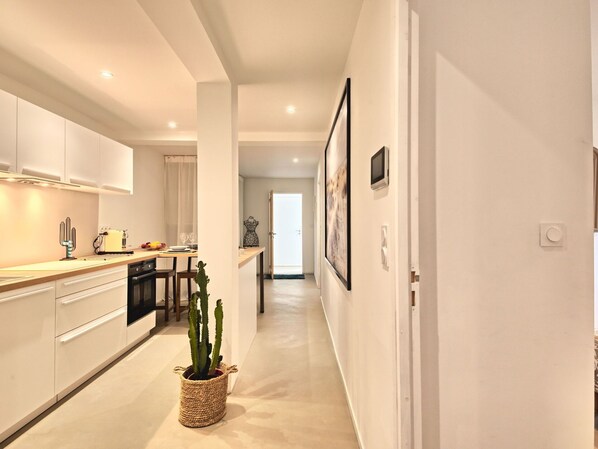 A modern kitchen with white cabinets, a dining area with a table and chairs, and a hallway with framed pictures.