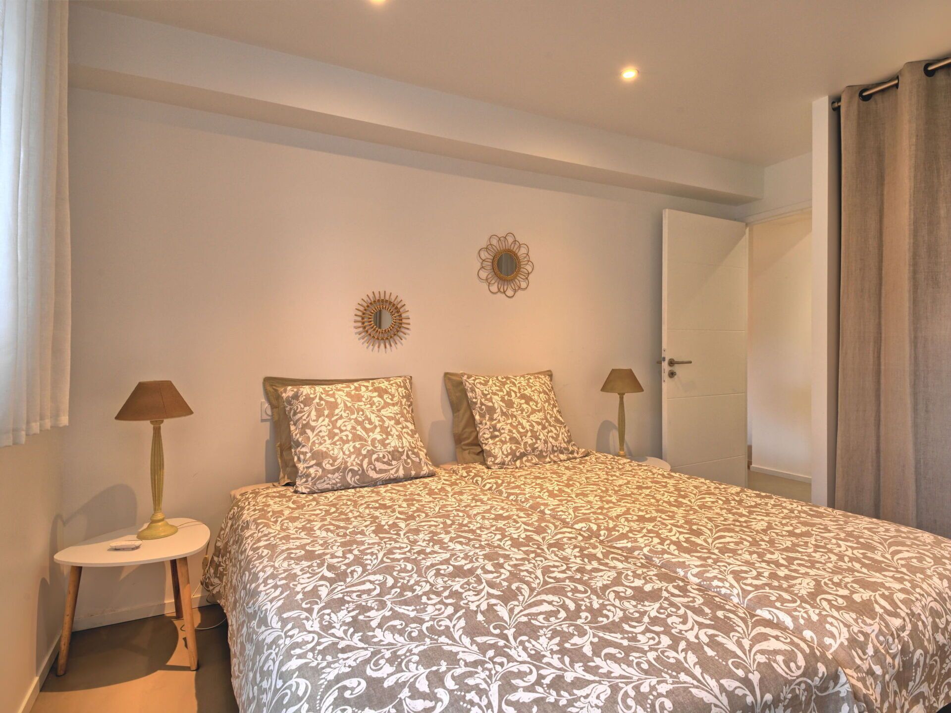 A bedroom with a bed, two bedside lamps, a small table, and a door.