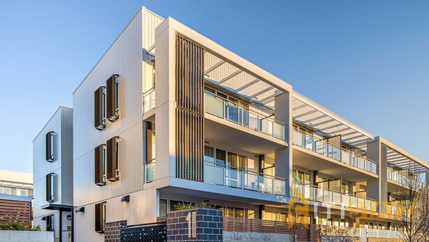 A modern multi-story residential building with a flat roof, large windows, and balconies.