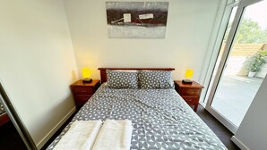 A neatly made bed with a geometric-patterned bedspread and two pillows, flanked by nightstands with lamps, in a room with a large window and a painting on the wall.