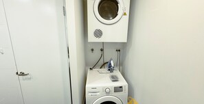 Un espace buanderie compact comprenant un lave-linge et un sèche-linge Samsung, tous deux blancs, dans une petite pièce dotée d’une porte blanche.