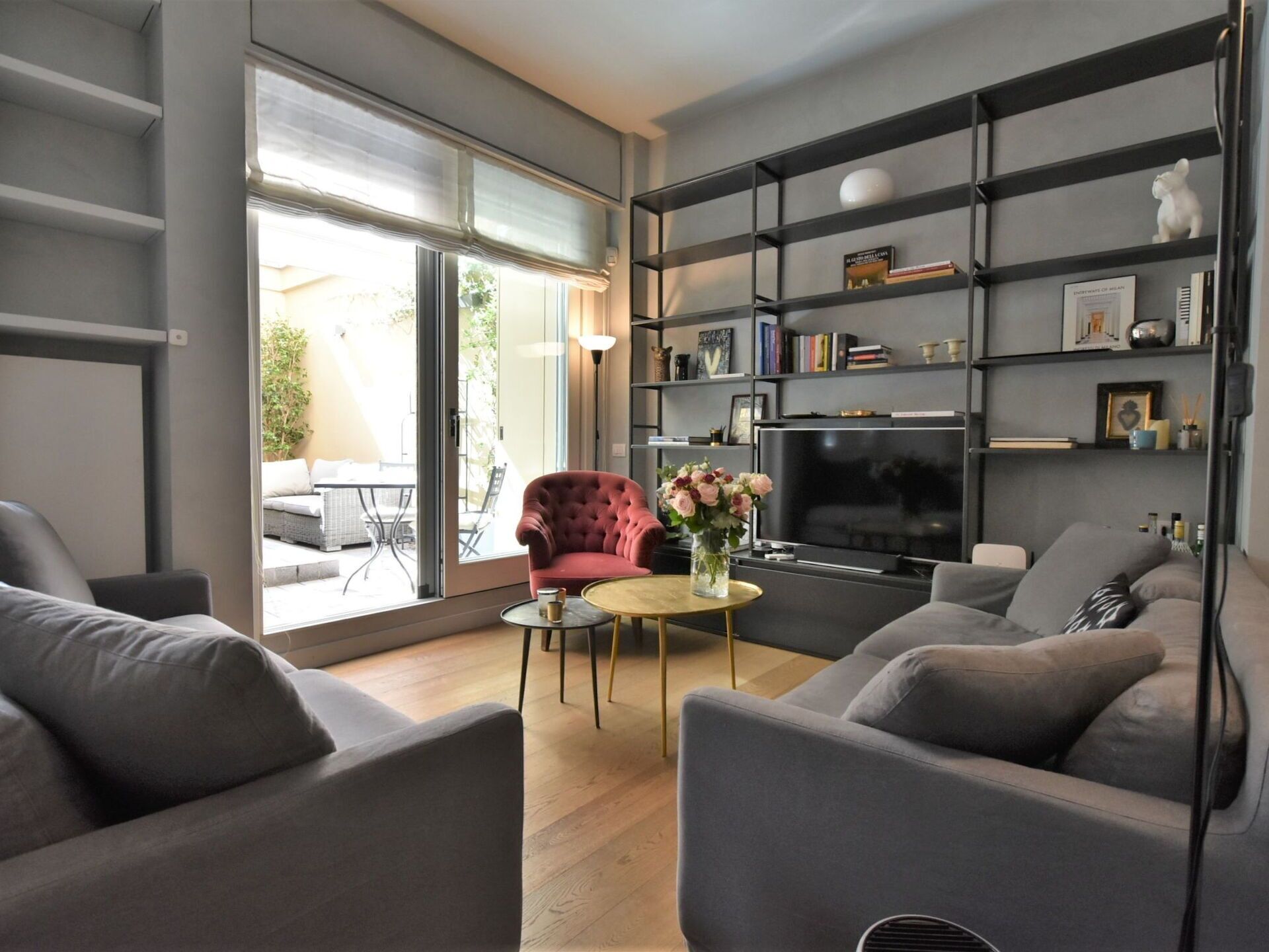 A modern living room with grey sofas, a red armchair, a TV, and a bookshelf.