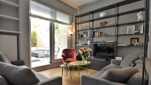 Un salon moderne avec des canapés gris, un fauteuil rouge, un téléviseur et une bibliothèque.