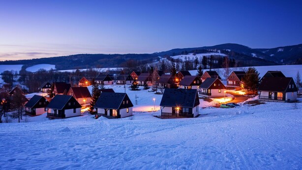Ein schneebedecktes Dorf im Abendlicht, die Häuser erstrahlen in warmem Licht.