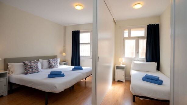 Ett hotellrum med två sängar, ett nattduksbord med en lampa, ett litet bord med en lampa och ett fönster med gardiner.