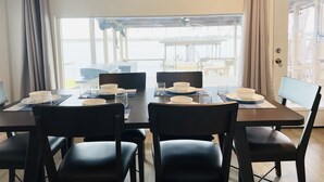 Comedor con una mesa lista para cuatro, sillas y vistas a un muelle y al agua.