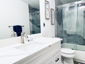 A modern bathroom with a large mirror, two sinks, a toilet, and a glass shower enclosure.