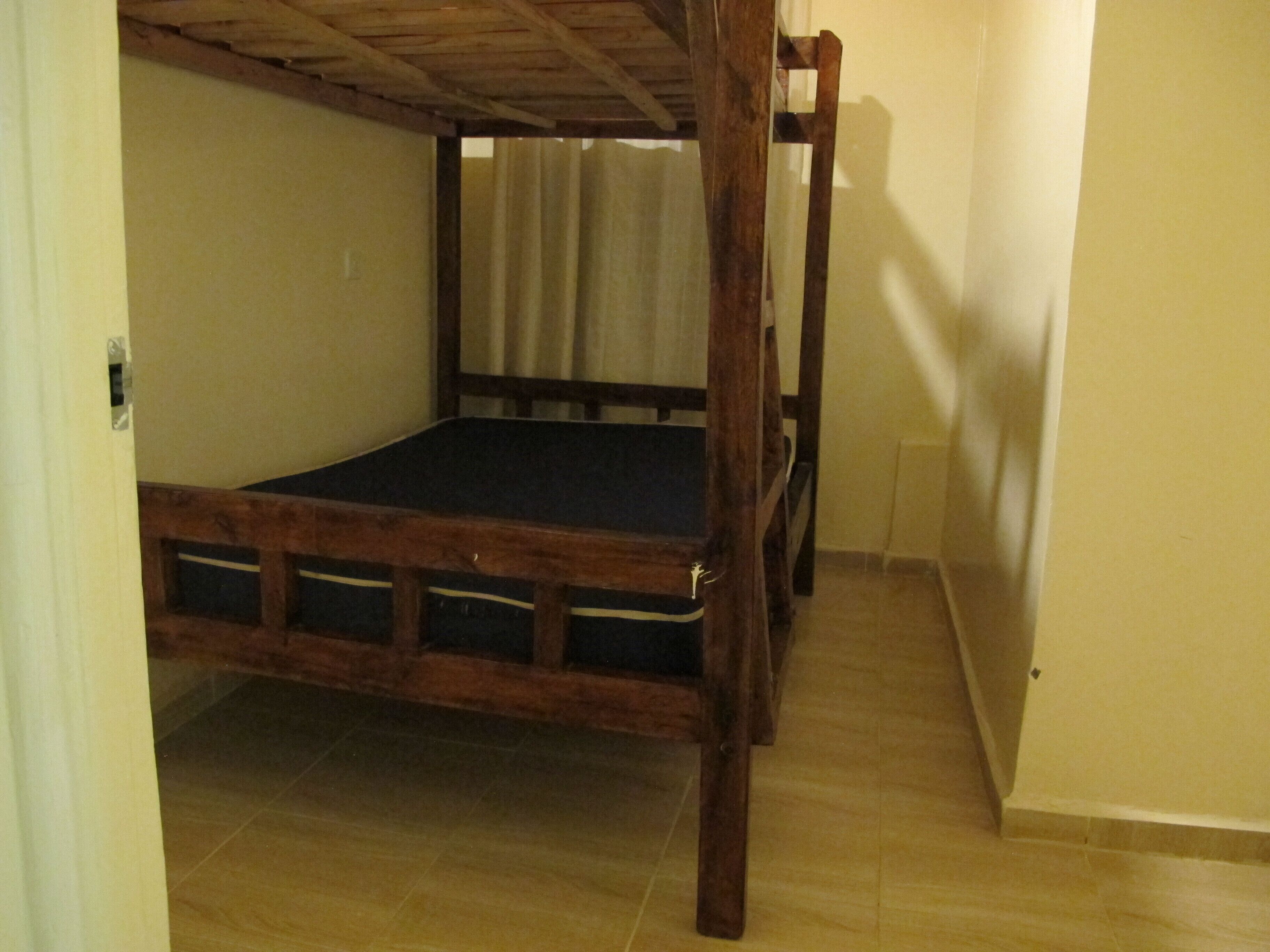 A room with a wooden bunk bed, a tiled floor, and a curtain on the window.