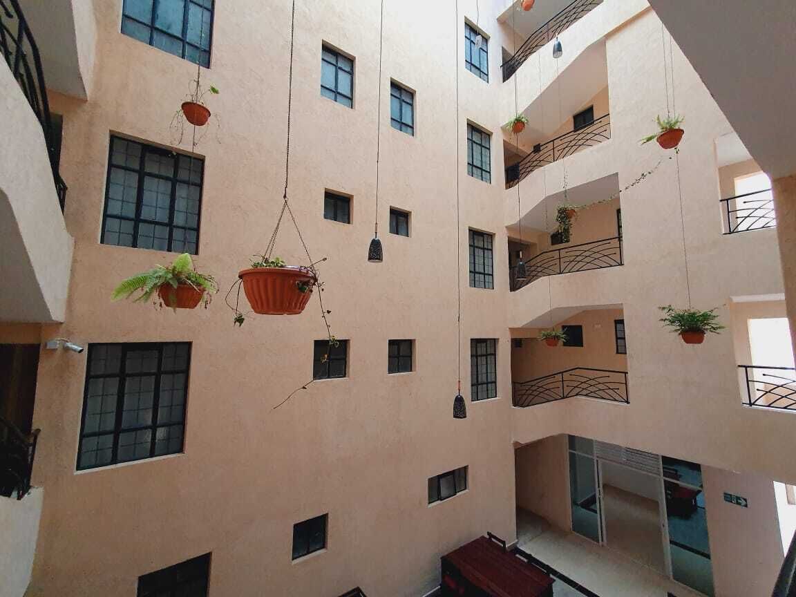 Un immeuble à plusieurs niveaux doté de balcons, de plantes suspendues et d’un espace central ouvert.