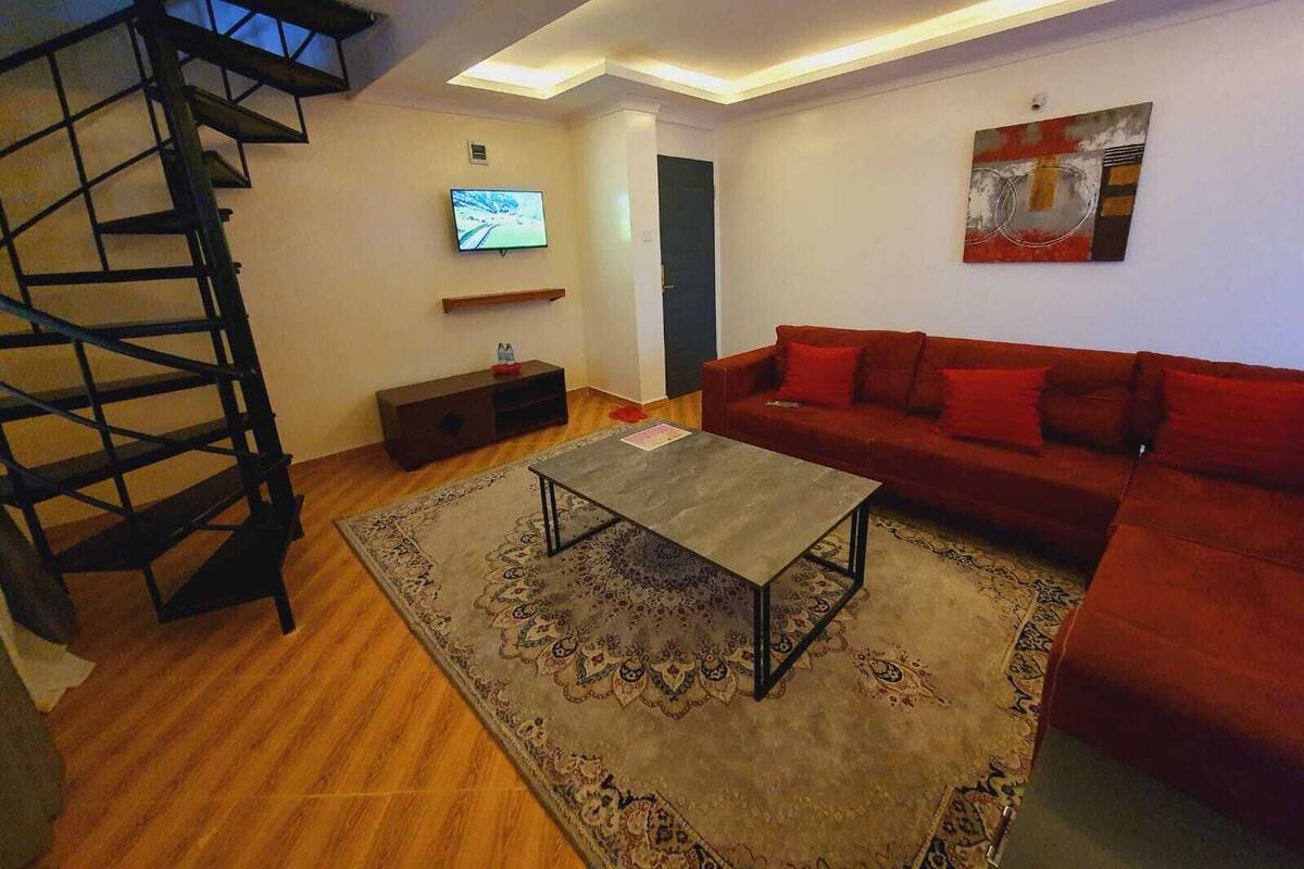 Uma sala de estar moderna com um sofá vermelho, uma mesa de centro, uma televisão e uma escada.