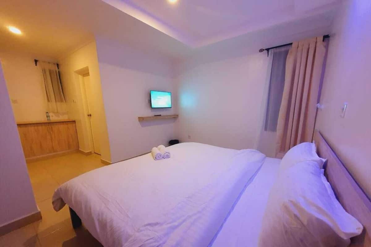 Quarto de hotel com uma cama, uma televisão sobre um suporte e um guarda-roupa de madeira.