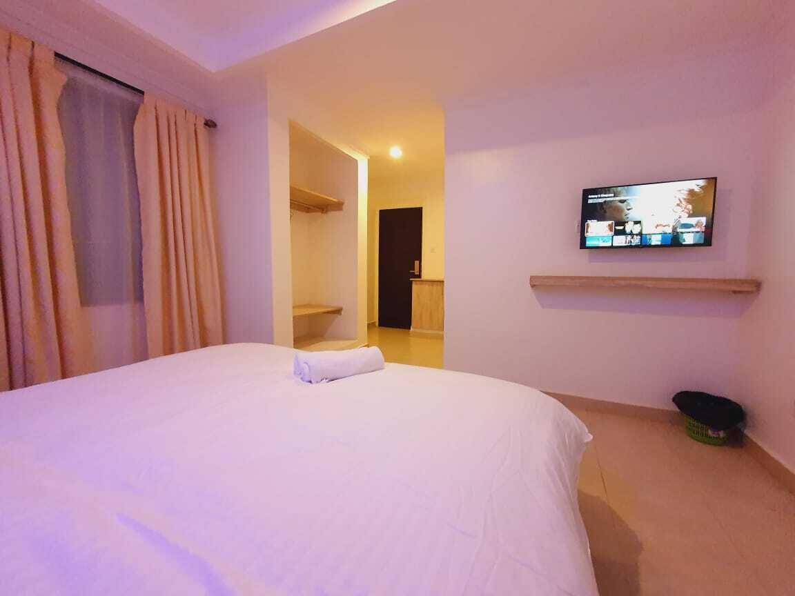 A hotel room with a bed, a television on the wall, and a small shelf.