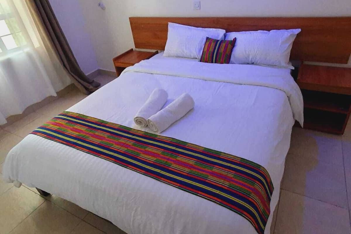 Cama bem arrumada com lençóis brancos e um cobertor listrado em cores vibrantes, cabeceira de madeira e travesseiro com padrão multicolorido.