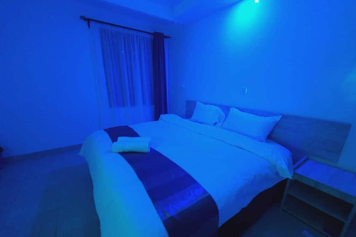 Quarto com cama, mesa de cabeceira e janela com cortinas.