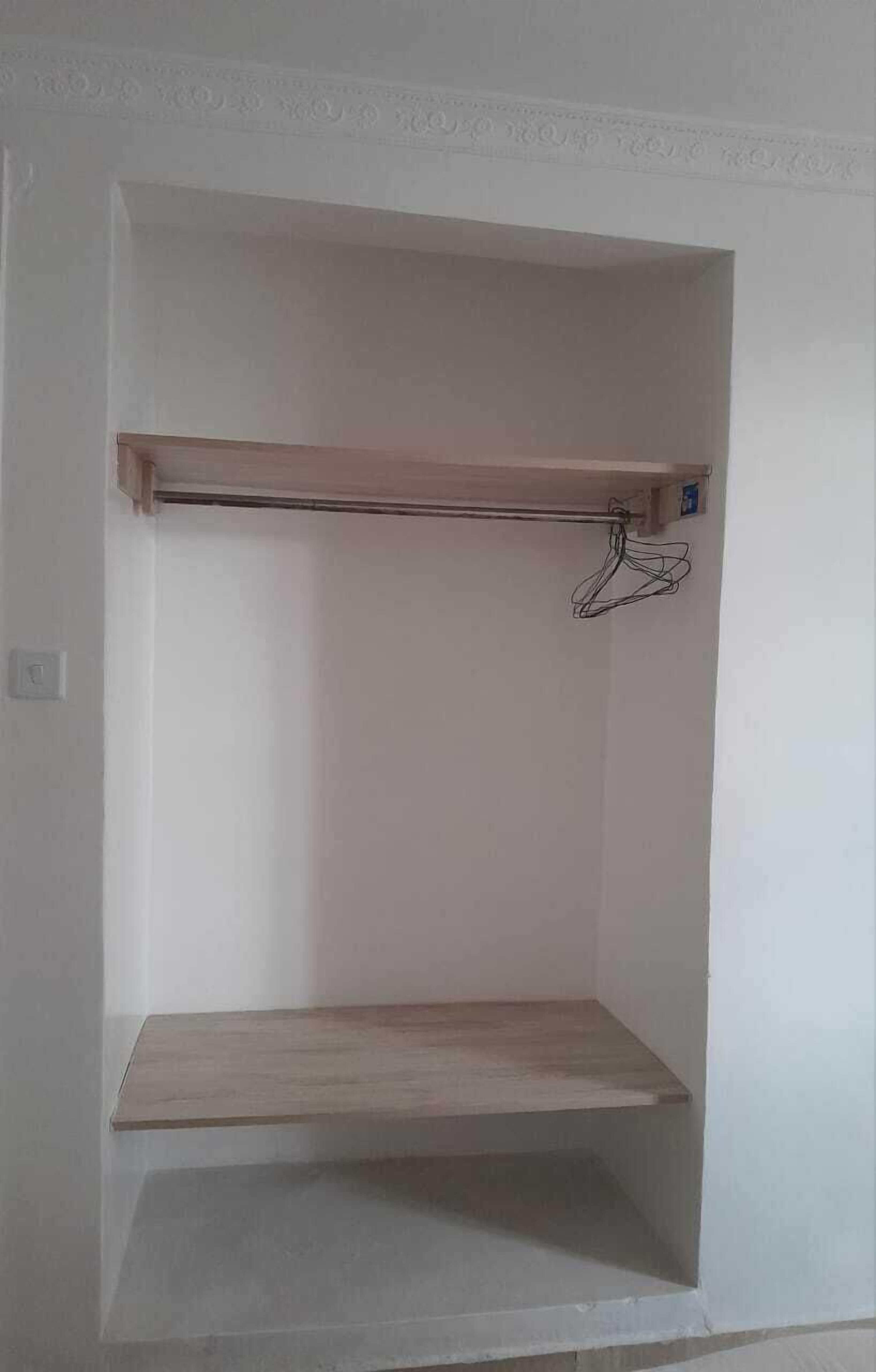 A room with a built-in wooden shelf and a hanging rack.