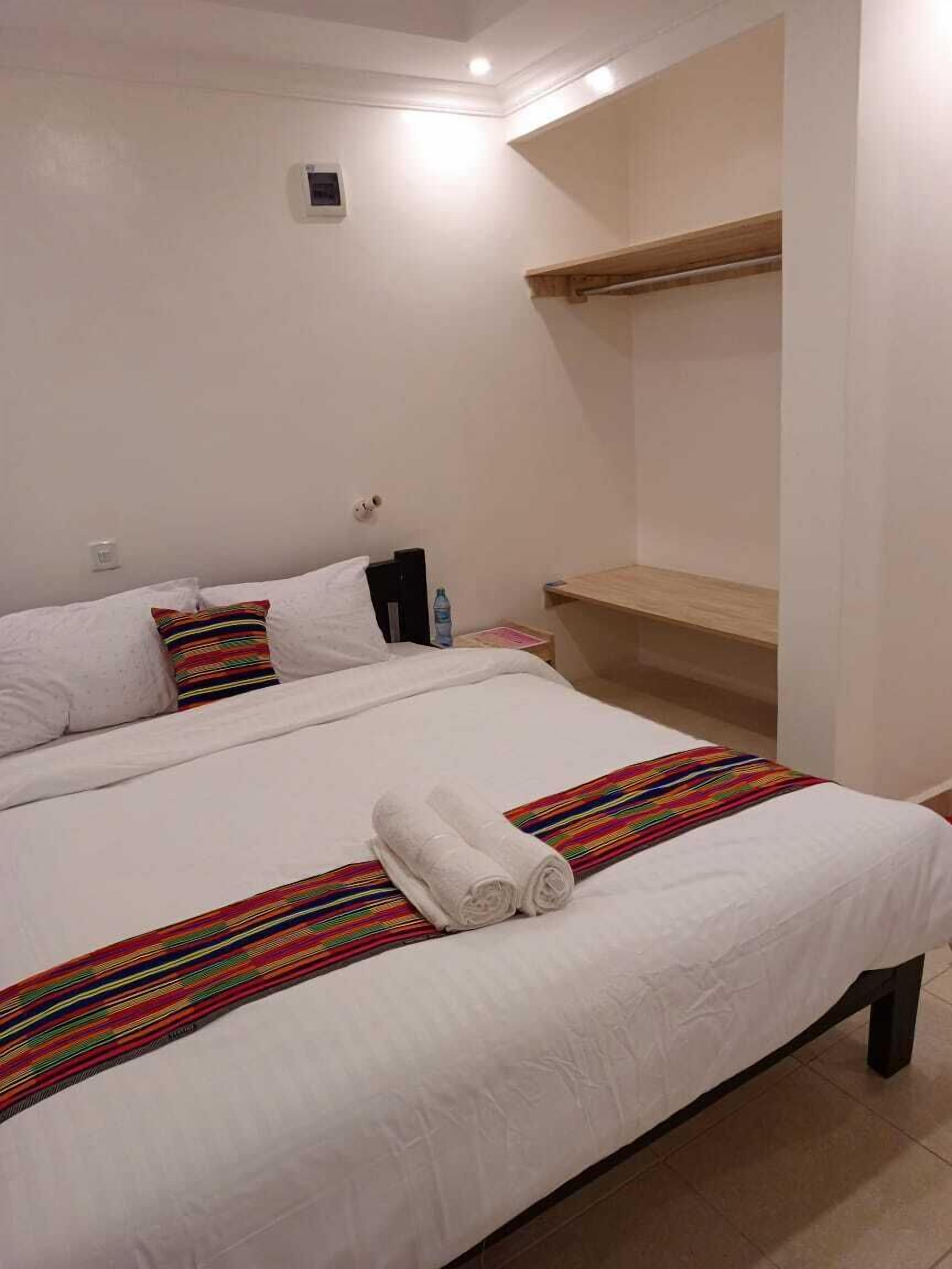 A hotel room with two beds, a wooden shelf, and a small wall-mounted device.