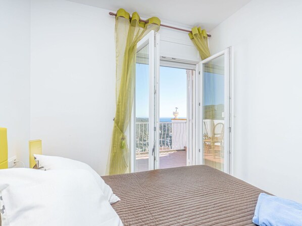 Un dormitorio con cama, ventana con cortinas translúcidas y balcón con vistas.