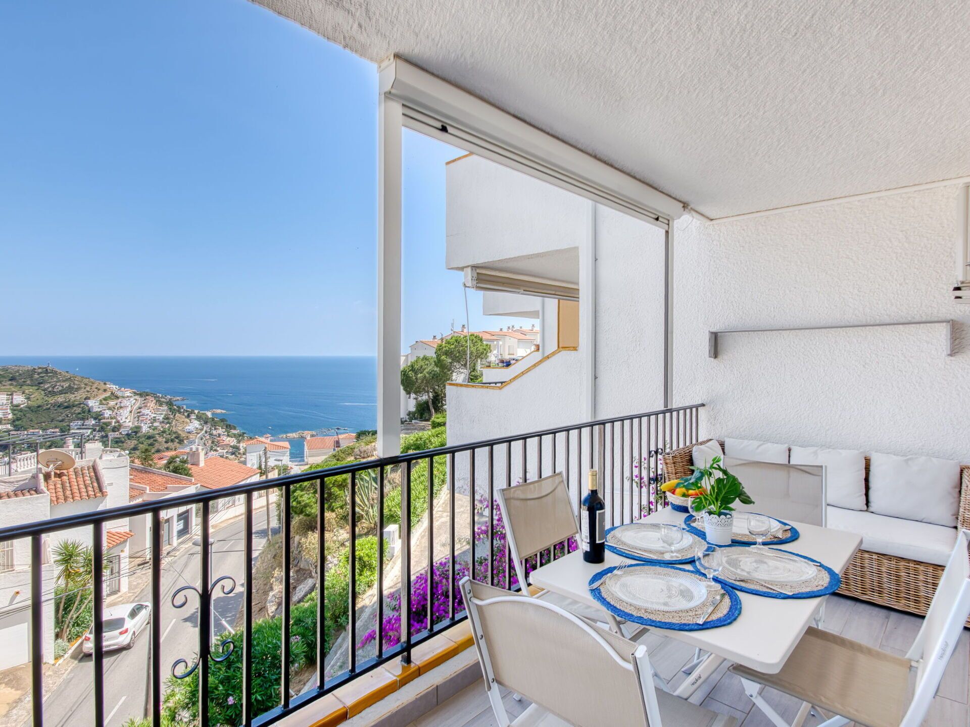 A balcony with a table set for dining, overlooking a coastal town and the sea.