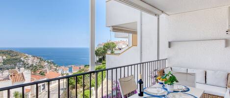 A balcony with a table set for dining, overlooking a coastal town and the sea.