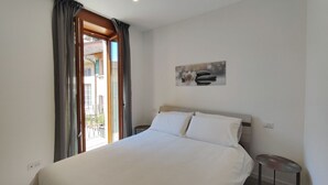 A bedroom with a bed, a small table, a painting on the wall, and a window with curtains.