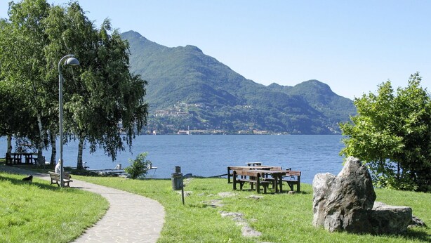 A paved path leading to a lakeside picnic area with benches and a large rock. - Cosy apartment in villa for 6 guests with WIFI, TV, patio and pets allowed (Dervio)
