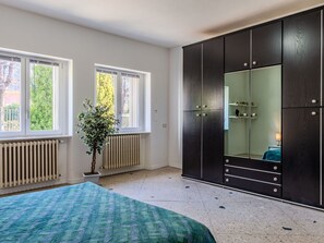 Et soveværelse med seng, stor garderobe, radiator, vindue og en potteplante.