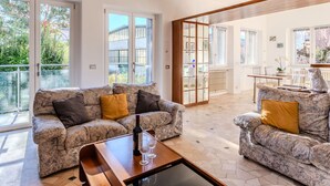 A spacious living room with two sofas, a coffee table, and a dining area with a table and chairs. Large windows provide natural light and views of the outside. - Lovely apartment in villa for 12 guests with A/C, WIFI, TV, patio and pets allowed (Dervio)