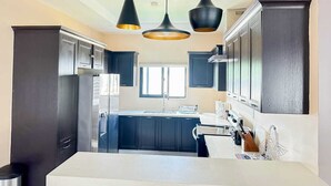 A modern kitchen with dark cabinetry, a central island, and pendant lighting. - Your cool oasis home away from home. Breath taking views for relaxation  (Ocho Rios)