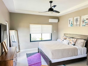 Ein Schlafzimmer mit einem Bett, einem Deckenventilator, einem Fenster mit Jalousien, einer Klimaanlage und einem Bild an der Wand.
