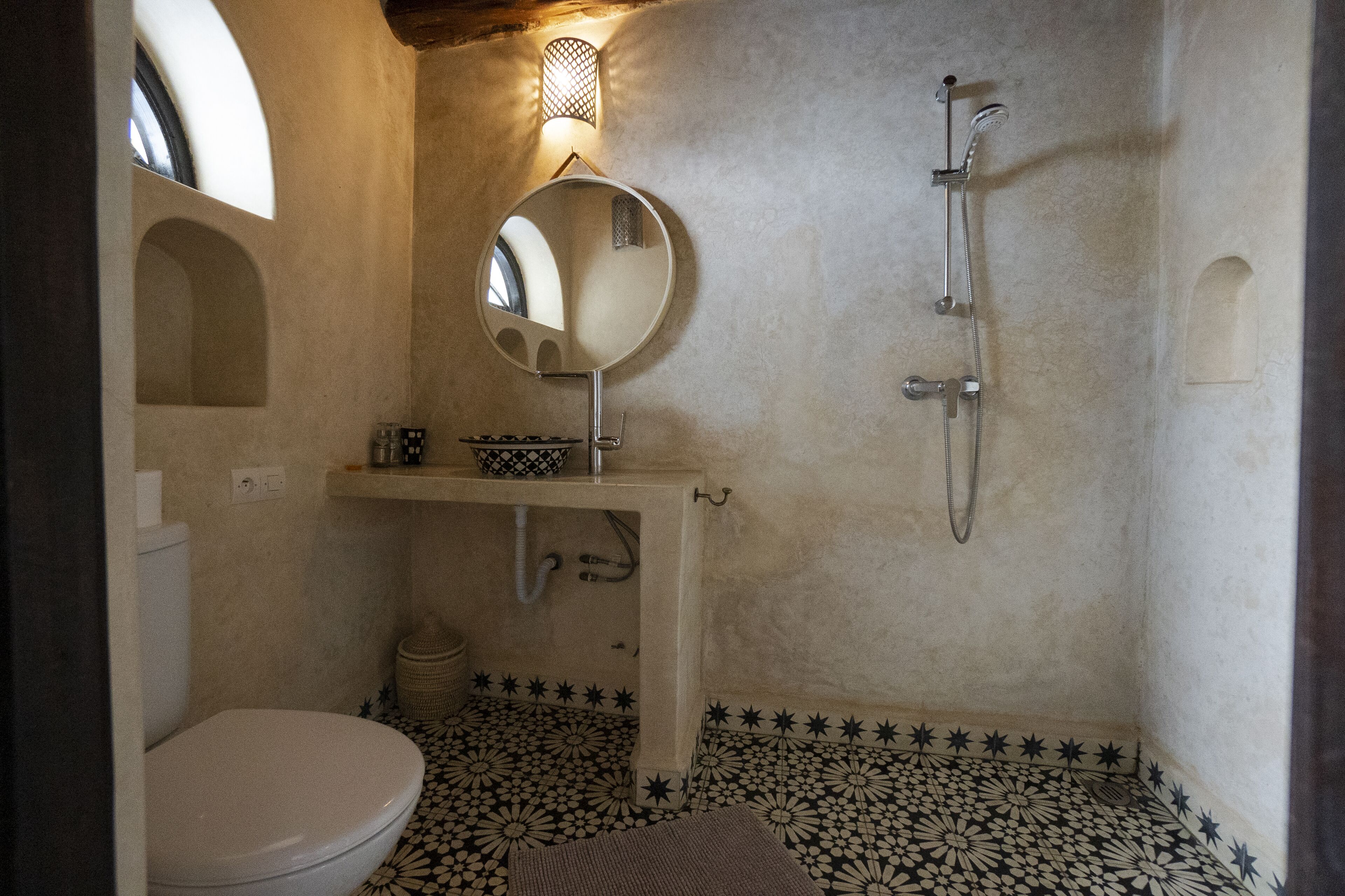 Un baño con inodoro, lavamanos con espejo, ducha y baldosas de suelo con diseño.