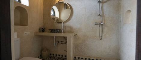 Un baño con inodoro, lavamanos con espejo, ducha y baldosas de suelo con diseño.