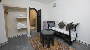 A room with a bed, a small table, a shelf with towels, and a patterned rug. - Dar Nor Riad  (Essaouira)