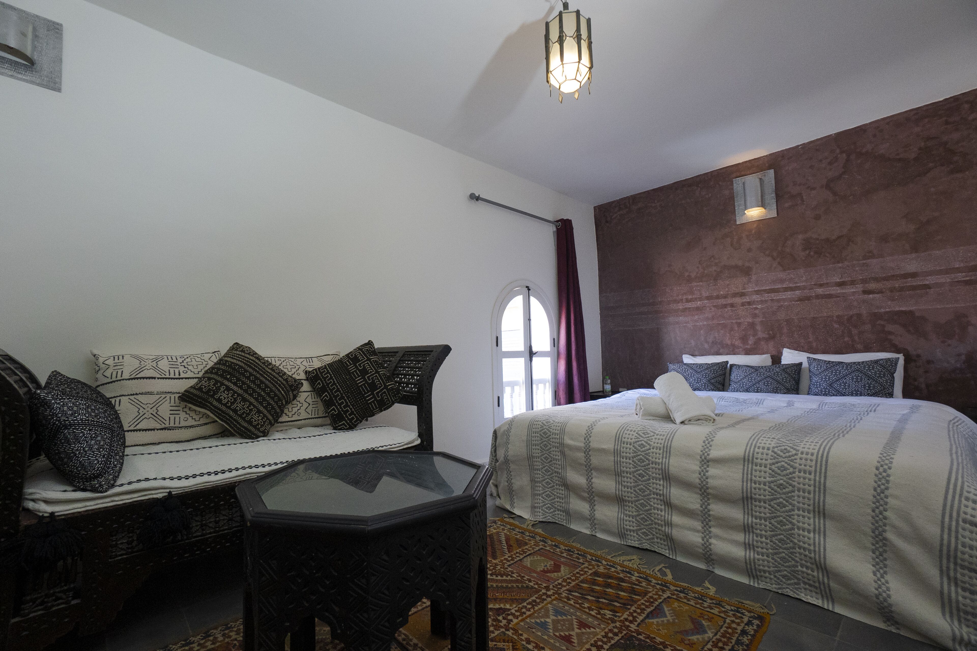 A bedroom with a bed, a sofa, a table, and a patterned rug.
