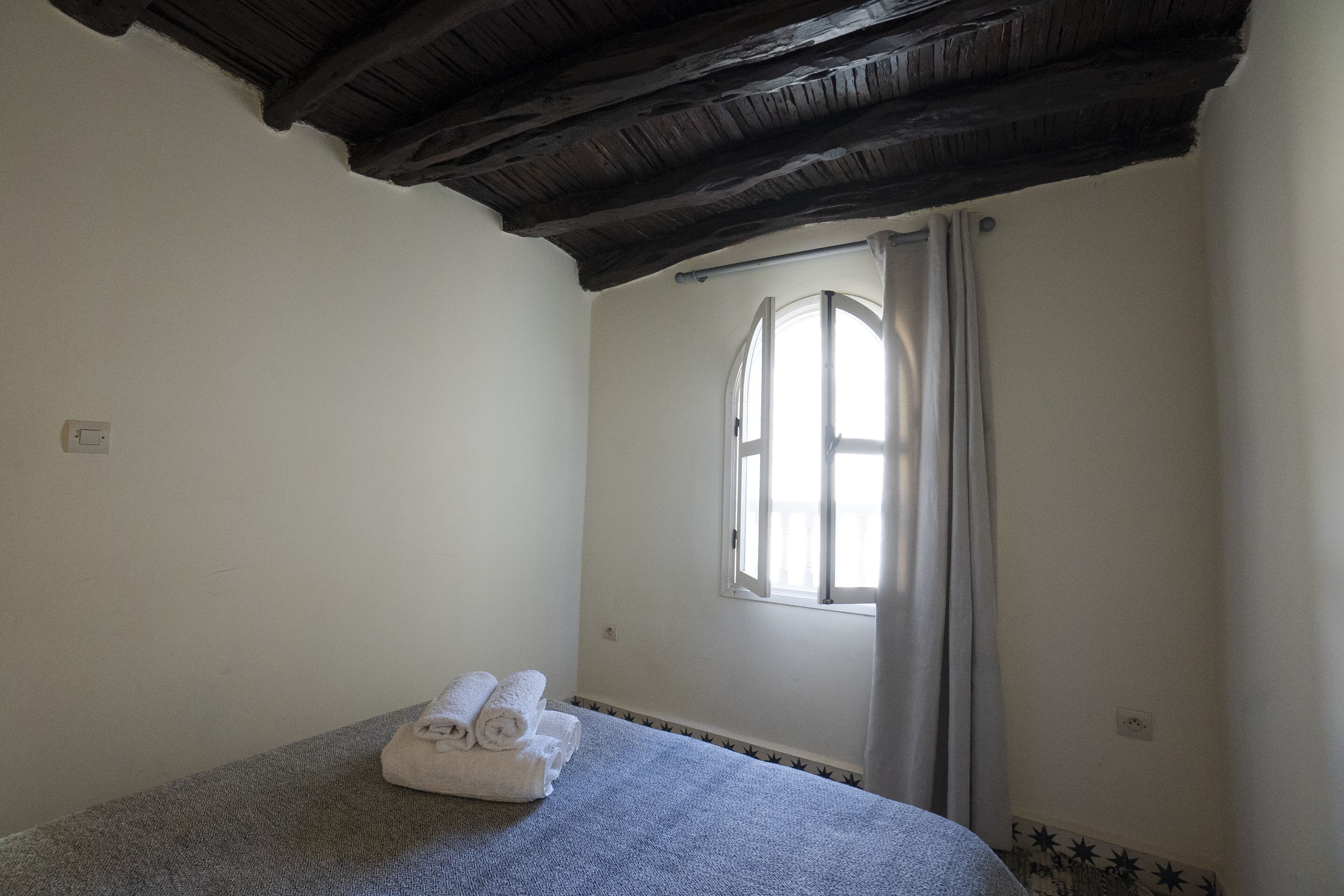A room with a bed, a window with curtains, and a towel on the bed.