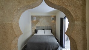 A bedroom with a stone archway, a bed with a patterned headboard, and two wall-mounted lights. - Dar Nor Riad  (Essaouira)