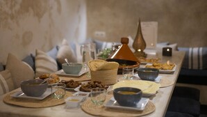 A dining table set with various dishes, including bowls, plates, and bread, in a room with a neutral color palette and a textured wall. - Dar Nor Riad  (Essaouira)