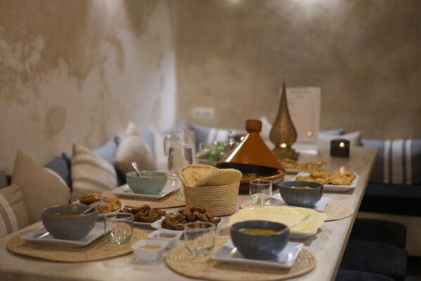A dining table set with various dishes, including bowls, plates, and bread, in a room with a neutral color palette and a textured wall. - Dar Nor Riad (Essaouira)
