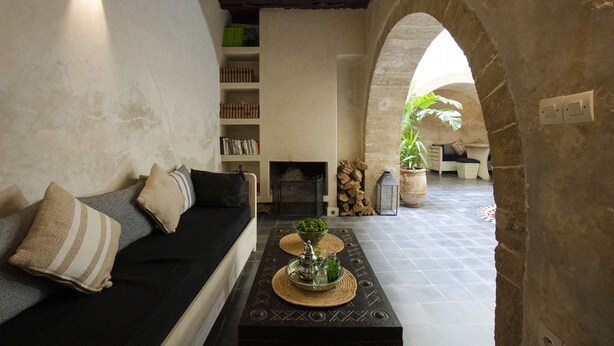A cozy living room with a black sofa, a fireplace, and a coffee table with decorative items. - Dar Nor Riad  (Essaouira)
