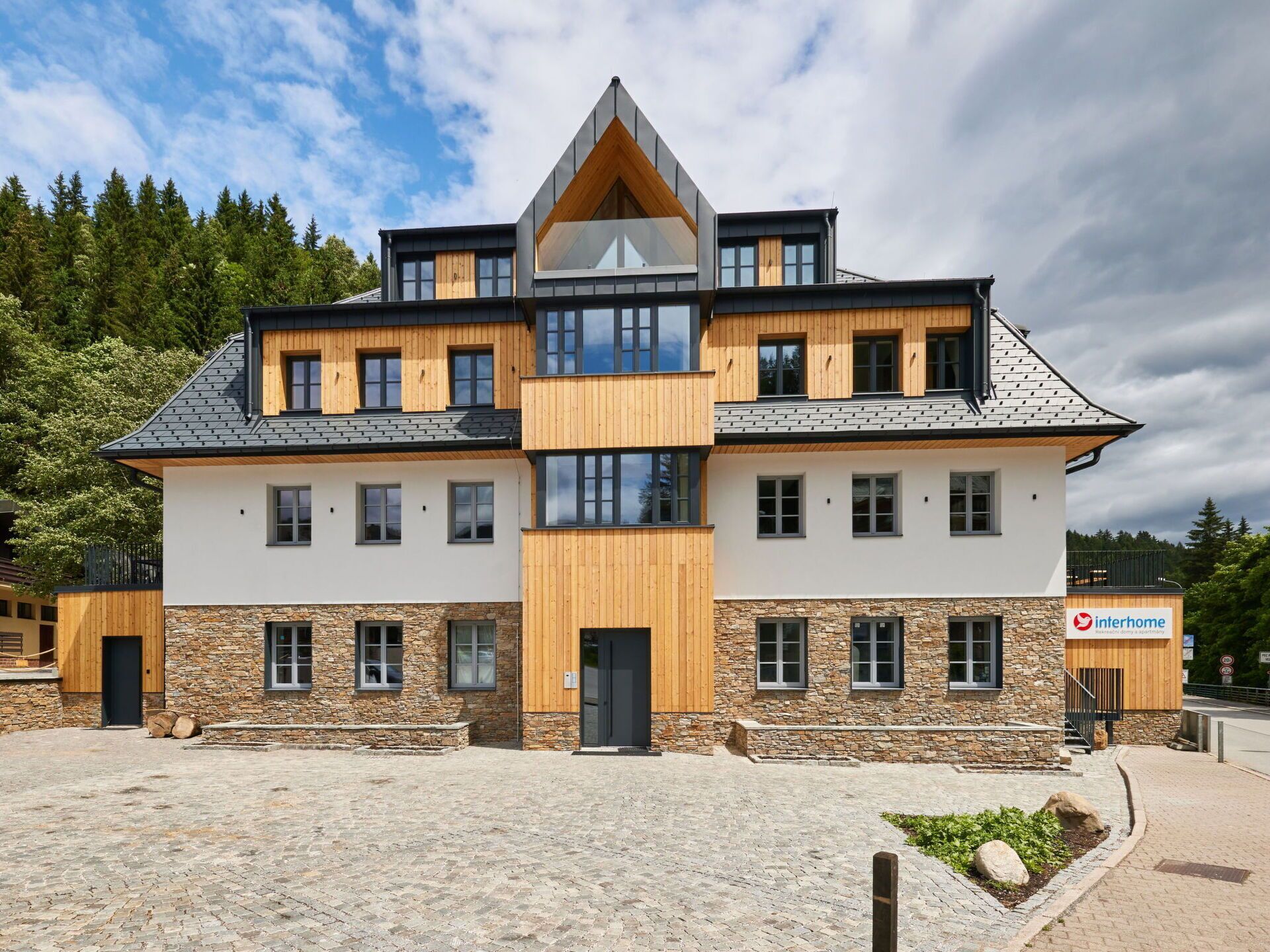 A modern multi-story building with a stone facade and wooden accents, featuring a prominent entrance and multiple windows.
