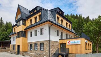 Un immeuble moderne à plusieurs étages, doté d’une combinaison de façades en bois et en pierre, d’un balcon et d’une petite annexe avec une enseigne.
