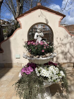 Ein Steinkunstwerk mit einer Statue, umgeben von verschiedenen Blumen und Pflanzen.