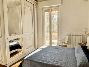 Quarto com cama, guarda-roupa, cadeira, radiador e janela com vista para o exterior.